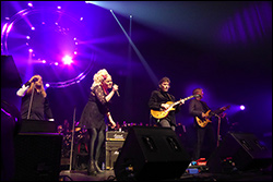 Steve Hackett Island. /></a>Am nächsten Tag ging es zum Inlandsflughafen von Reykjavik, der am Stadtrand liegt. Die Hacketts und die Band hatten schon einen früheren Flug genommen, aber es gehen täglich mehrere Flüge zwischen Reykjavik und Akureyri hin und her. Es sind kleine Propellermaschinen mit vielleicht 50 Passagieren Fassungsvermögen. Man holt sich zwar am Flughafenschalter die Bordkarte ab, aber es gibt dort keinerlei Sicherheitskontrollen. Man geht einfach durch eine Tür auf das Rollfeld und steigt in die Maschine ein. Wir hatten Glück mit dem Wetter und konnten den Flug bei blauem Himmel genießen und somit einen Blick auf endlose weiße Landschaften. Es war zwar ein Vulkan aktiv (Bárðarbunga), aber den haben wir nicht sehen können und man hätte ihn aus der Ferne wohl auch nicht von Wolken unterscheiden können, da er nur mäßig aktiv gewesen sein soll. Akureyri liegt in einem langgestreckten Fjord und es war schon kurz nach Sonnenuntergang, als wir dort landeten. Während in Reykjavik eher wenig Schnee lag, gab es hier im noch höheren Norden deutlich mehr davon und es war ca. -5 °C kalt, dafür aber nicht ganz so windig. Nach der Landung haben wir erst kurz unser Apartment bezogen, das sogar noch geräumiger war als das in Reykjavik, und sind dann zur Konzerthalle gegangen, die quasi um die Ecke lag. Die Halle, „Hof“ genannt, fasst gut 500 Zuschauer, ist aber topmodern und gut ausgestattet. Nachdem wir dort im Foyer erst mal mit den Hacketts gespeist hatten, sind wir direkt mit ihnen in den Saal gegangen, wo es noch einen letzten Soundcheck gab. Für diese Show hatte ich einen Platz in der 2. Reihe ergattert, aber ganz außen. Es gab aber auch weiter hinten unterhalb des Oberrangs ein paar freie Plätze, mehr in der Mitte, wo ich mich dann niederließ und den noch besseren Sound (im Vergleich zum Vortag) genießen konnte. Die Setliste war genau die gleiche, auch die Besetzung, nur dass sich Chor und Orchester teilweise aus anderen Musikern von Akureyri zusammensetzten.</p>
<p> <a title=